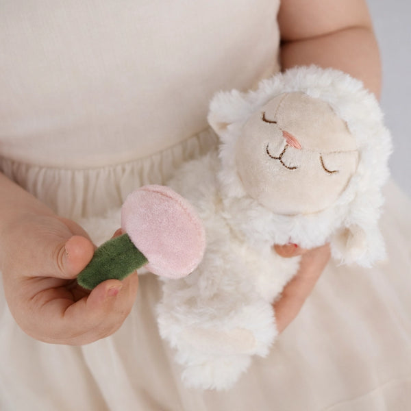Person holding a soft toy with a pink flower and green stem against a neutral background