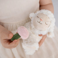 Person holding a soft toy with a pink flower and green stem against a neutral background