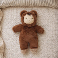 Small plush toy in a brown outfit lying on a textured beige surface