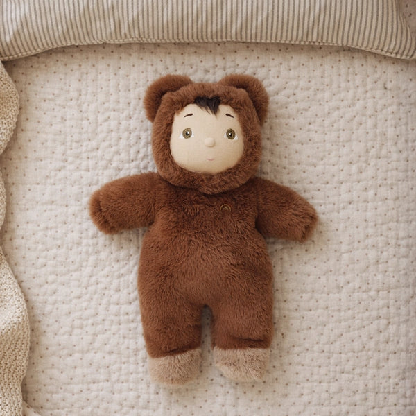 Small plush toy in a brown outfit lying on a textured beige surface