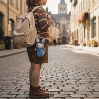 Person standing on a cobblestone street with a backpack and blue plush toy, in front of a historic building.