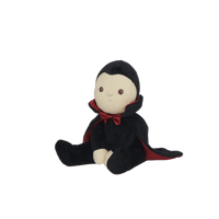 Stuffed toy dressed as a vampire with a black cape and red collar on a white background