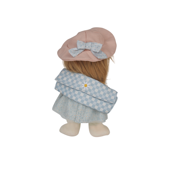 Doll wearing a pink hat with a bow and a blue checkered dress on a white background