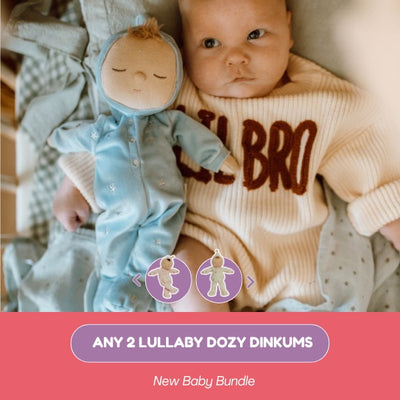 Baby in a 'LIL BRO' onesie with a blue baby doll, surrounded by soft textures.