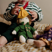 Child holding a doll with a yellow hat and green coat on a checkered blanket