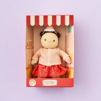 Doll in a box with a red and white striped roof on a light purple background